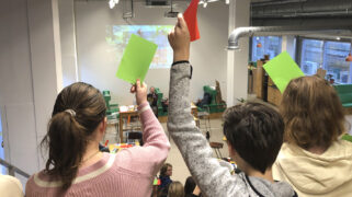 Leerlingen van Yuverta beantwoorden vragen door kaartjes in de lucht te steken.